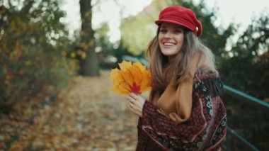 Merhaba sonbahar. 40 yaşında, kırmızı şapkalı, güz yapraklı ve fularlı bir kadın şehir parkında yürüyor..