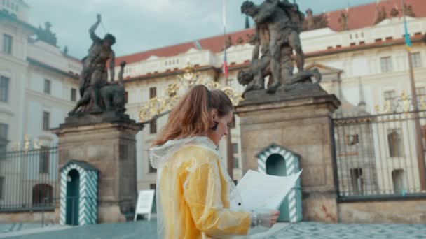 捷克共和国布拉格 身穿黄色衬衫和雨衣 头戴智能手机和耳机 对着城市全景微笑的年轻旅行者 — 图库视频影像