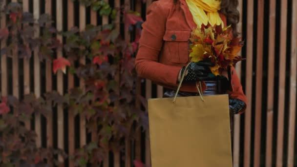 10月份 全市穿着橙色风衣 头戴购物袋 头戴秋天黄叶的年轻女性的衣服 — 图库视频影像
