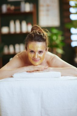 Sağlık hizmeti zamanı. Masaj maskesinin üzerinde altın kozmetik maskesiyle spa salonundaki rahat modern kadın..