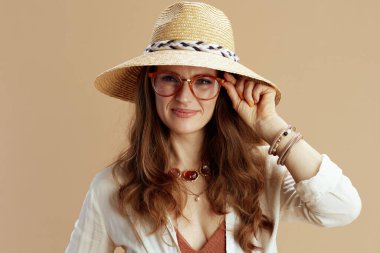 Plaj tatili Beyaz bluz ve şort giyen, gözlüklü, hasır şapkalı, bej arka planda sırıtan moda bir kadın..