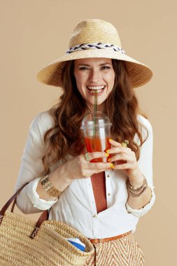 Plaj tatili Beyaz bluz içinde mutlu zarif bir kadın ve bej arka planda saman torbası, havuç suyu ve yaz şapkası olan bir şort..