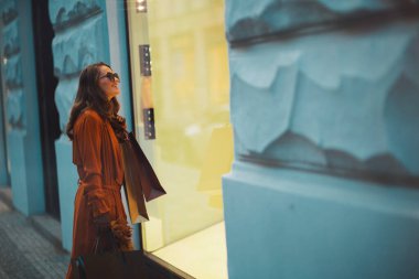 Merhaba sonbahar. Şehirde alışveriş torbaları ve sonbahar sarısı yapraklarıyla turuncu trençkotlu zarif bir bayan..