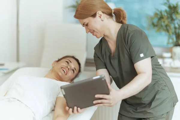 Healthcare time. smiling massage therapist woman in massage cabinet with client and digital tablet.