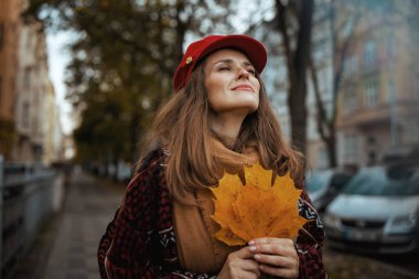 Merhaba sonbahar. Şehirde sonbahar yaprakları ve eşarplarıyla kırmızı şapkalı, orta yaşlı, rahat bir kadın..