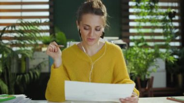 Modern yeşil ofiste sarı kazaklı, mutlu, küçük işletme sahibi bir kadın web kamerası toplantısı yapıyor ve çizelgeleri gösteriyor..