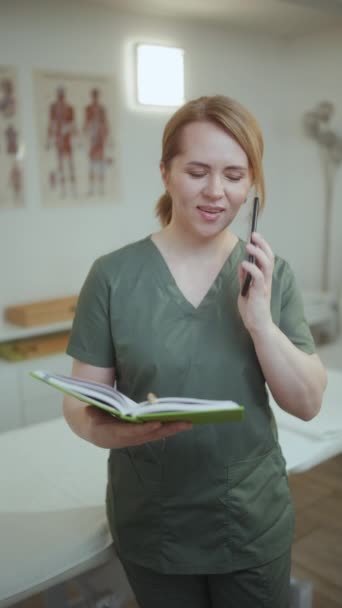 卫生保健时间 快乐的女性医疗按摩师在按摩室里带着笔记本用智能手机聊天 — 图库视频影像
