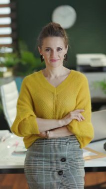 smiling elegant small business owner woman in yellow sweater standing in the modern green office.