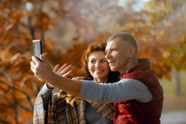 Merhaba sonbahar. Parktaki mutlu romantik çift akıllı telefon kullanıyor ve selfie çekiyor..