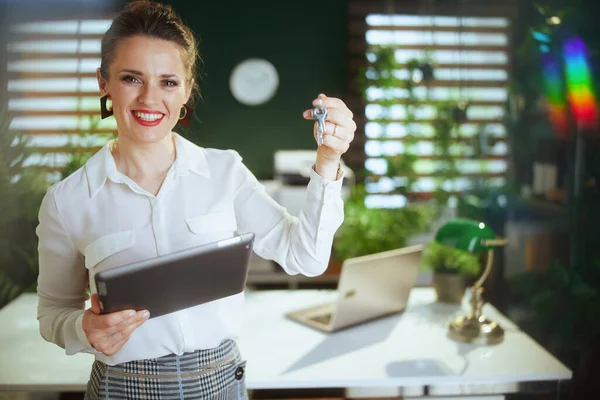 Sustainable real estate business. happy modern woman realtor in modern green office in white blouse with digital tablet and keys.