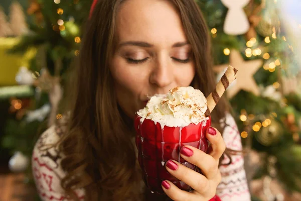 圣诞节的时候在现代房子的圣诞树旁 穿着现代女性的衣服 喝着节日热巧克力鸡尾酒 — 图库照片