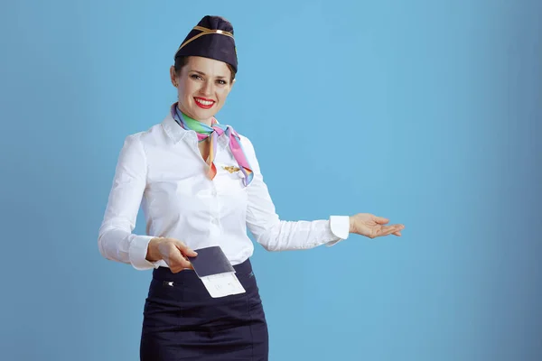smiling stylish flight attendant woman isolated on blue background in uniform with flight tickets and passport.