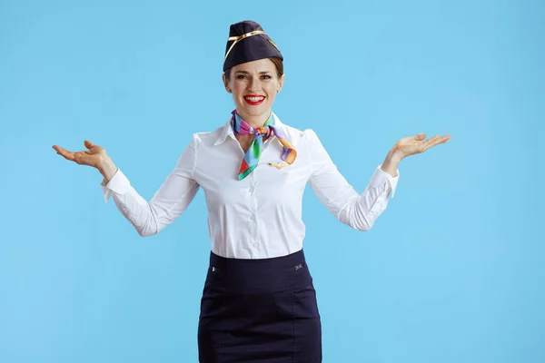 happy elegant female air hostess isolated on blue background in uniform presenting something on empty palm.