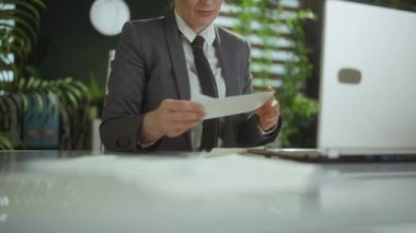 Yeni bir iş. Modern yeşil ofiste, gri takım elbiseli, modern orta yaşlı kadın işçi belgeleri fırlatıyor..