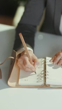 Sürdürülebilir iş yeri. Yeşil ofisteki gri takım elbiseli orta yaşlı kadın çalışana yakın çekim. Not defterinde yazıyor..