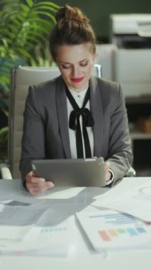 Sürdürülebilir iş yeri. Tablet kullanarak modern yeşil ofiste gri takım elbiseli gülümseyen modern kadın işçinin portresi..