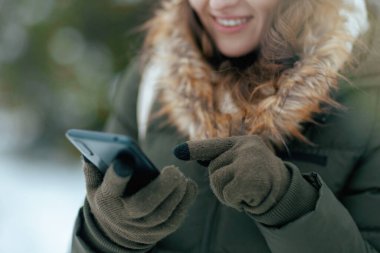 Kışın şehir parkında, akıllı telefon uygulamaları kullanarak eldivenli mutlu bir kadına yakın çekim..