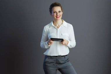 Beyaz bluzlu mutlu kadın işçi gri arka planda akıllı telefondan mesajlar yazıyor..