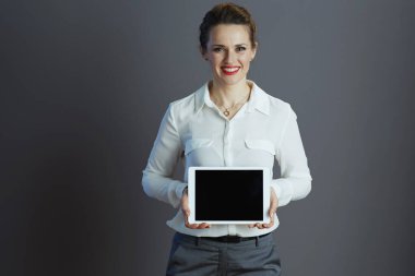 Mutlu modaya uygun 40 yaşında beyaz bluzlu kadın çalışanı gri arkaplanda izole edilmiş tablet bilgisayar ekranı gösteriyor..