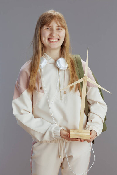 happy modern teen girl in beige tracksuit with headphones and windmill against grey.