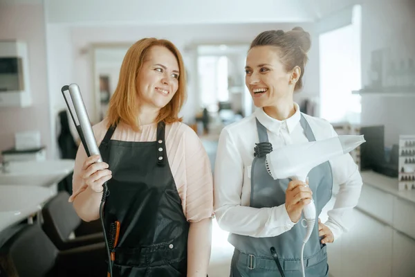Счастливые Две Женщины Парикмахеры Форме Современной Студии Красоты Выпрямителем Волос — стоковое фото