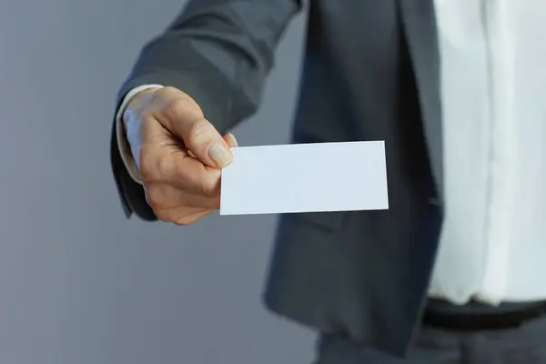Closeup on middle aged woman employee in gray suit with business card isolated on gray.