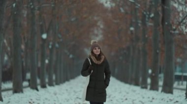 Mutlu, orta yaşlı, yeşil ceketli, kahverengi şapkalı bir kadın kışın şehir parkında bereli..