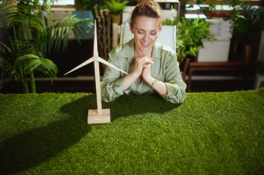 Eko zamanı. Yeşil bluzlu zarif küçük işletme sahibi kadın modern yeşil ofiste yel değirmeni ile