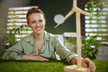 Gülümseyen küçük işletme sahibi, yeşil bluzlu, modern yeşil ofisli, yel değirmenli bir kadın.