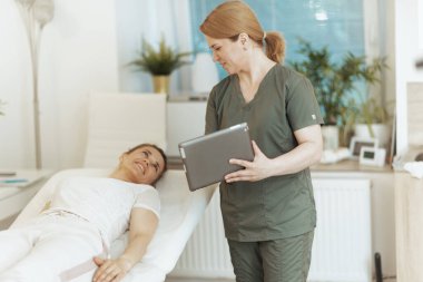 Sağlık hizmeti zamanı. Müşteri ve tabletle masaj dolabında gülümseyen kadın masaj terapisti..