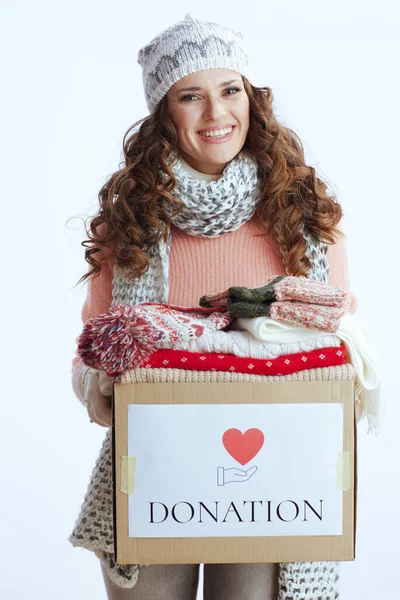 Hello winter. smiling modern 40 years old woman in sweater, mittens, hat and scarf isolated on white background with donation box.