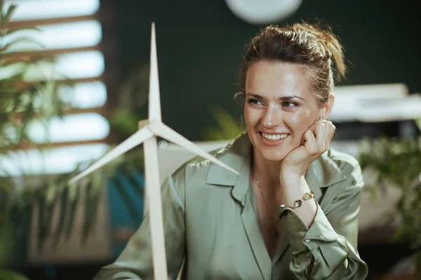 Eco trends. happy elegant middle aged small business owner woman in green blouse in modern green office with windmill