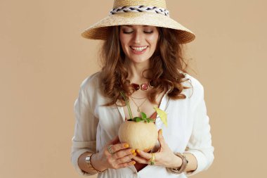 Plaj tatili Beyaz bluz ve bej üzerine izole edilmiş, Hindistan cevizi kokteyli ve yaz şapkalı mutlu orta yaşlı ev hanımı..