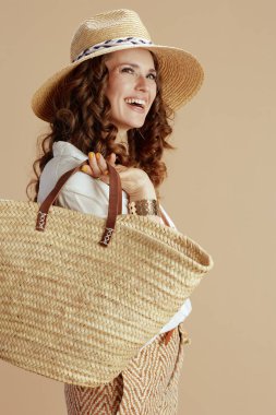 Plaj tatili Beyaz bluz ve şortlu mutlu modern ev hanımı saman çantalı ve hasır şapkalı bej üzerine izole edilmiş..