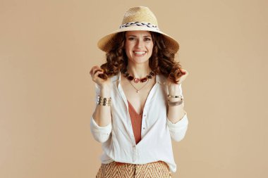 Plaj tatili Gülümseyen orta yaşlı beyaz bluzlu kadın ve saman şapkalı bej arkaplan şortlu..