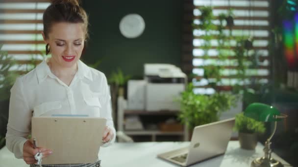 持続可能な不動産ビジネス クリップボード付きの白いブラウスの現代緑のオフィスで現代の女性のリアクターを微笑みます — ストック動画
