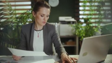 Sürdürülebilir iş yeri. Modern yeşil ofisteki gülümseyen modern iş kadını ellerini uzatan dizüstü bilgisayarla.