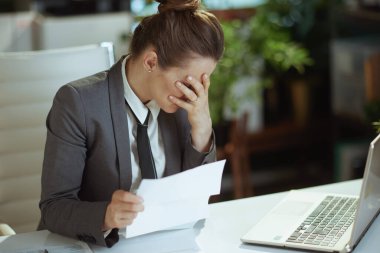 Yeni bir iş. Gri takım elbiseli, modern yeşil ofisteki modern orta yaşlı kadın çalışanın işten çıkarılma mektubuyla strese girmesi.
