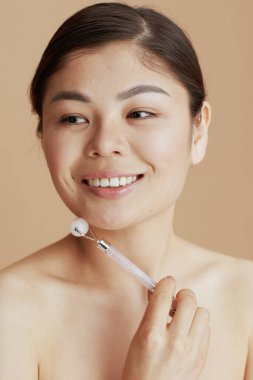 Bej arka planda tekerlekli masaj aleti olan genç Asyalı kadın..