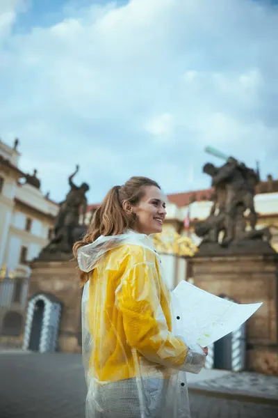 布拉格城堡附近一名身穿黄色上衣和雨衣的快乐的现代女性游客带着地图来到了布拉格 — 图库照片