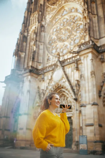 happy trendy woman in yellow blouse in Prague Czech Republic sightseeing, listening to an audio guide on smartphone app, talking on a smartphone and walking.