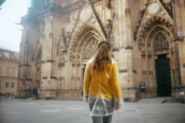 プラハチェコ共和国の黄色いブラウスとレインコートの女性の後ろから見た遊歩道を楽しむ — ストック写真