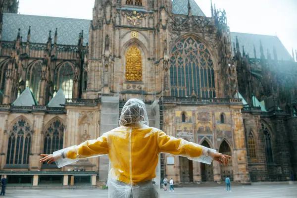 stock image Seen from behind woman in yellow blouse and raincoat in Prague Czech Republic sightseeing and rejoicing.