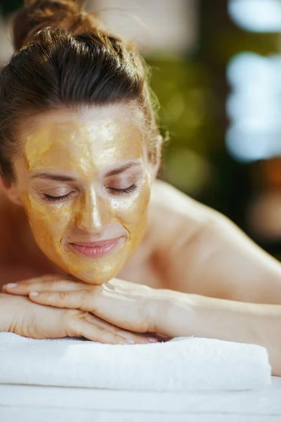 Healthcare time. relaxed modern female in massage cabinet with golden cosmetic mask on face laying on massage table.