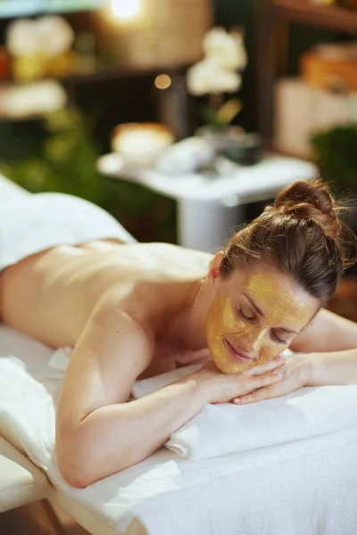 Healthcare time. relaxed modern woman in massage cabinet with golden cosmetic mask on face laying on massage table.