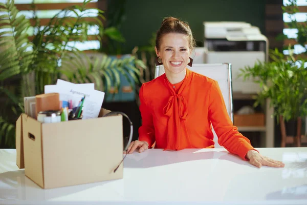 New job. smiling modern woman worker in modern green office in red blouse with personal belongings in cardboard box.