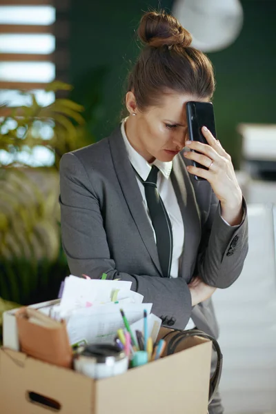 新しい仕事 ダンボール箱およびスマートフォンの個人的な持ち物が付いている灰色のビジネス スーツの現代緑のオフィスの不幸な現代女性の従業員 — ストック写真