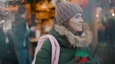 Kış fuarında yeşil ceketli ve kahverengi şapkalı gülümseyen modern bir kadın..