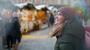 Şehirdeki kış fuarında yeşil ceketli ve kahverengi şapkalı mutlu modern kadın....