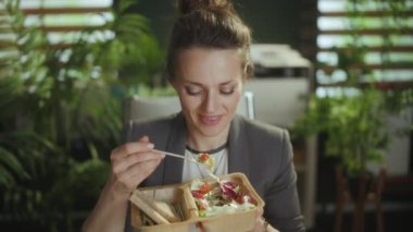 Sürdürülebilir iş yeri. Modern yeşil ofiste gri takım elbiseli, modern orta yaşlı muhasebeci kadın salata yiyor..
